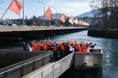 Diverse group of people in World Cancer Day branded hoodies posing outdoors in front a bridge lined with World Cancer Day flags