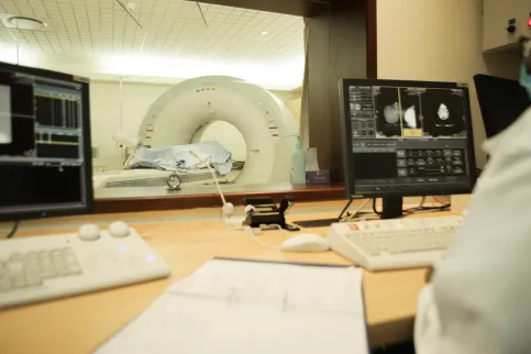 An African woman in lab coat checking scans as a patient goes through a scanning machine