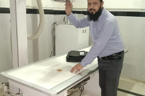 Middle Eastern man in shirt and trousers in front of a radiotherapy machine