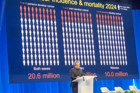 Man at podium giving a slide show presentation of cancer incidence and mortality