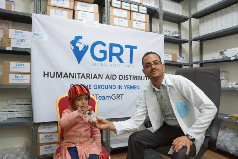 Doctor in Yemen posing with a child living with cancer in front of a billboard for aid distribution by the Global Relief Fund (GRT)