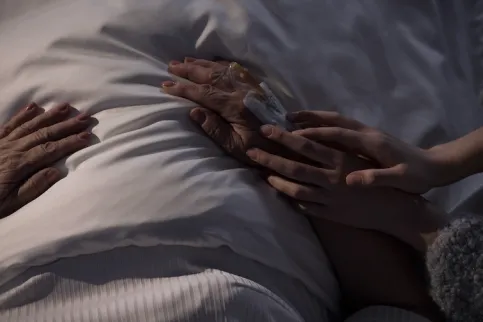 Close up of a hand touching a patient's hand on a bed