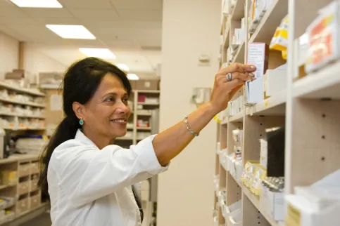 Woman in white blouse reaching for medication on a shelf