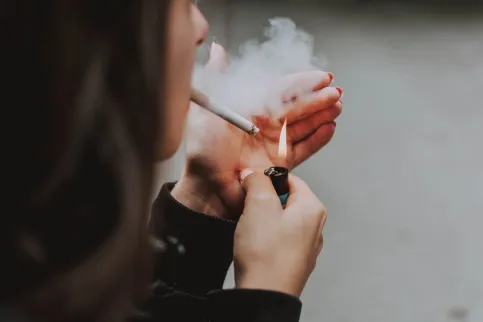 Over the shoulder shot of a young woman cupping a lighter to light a cigarette