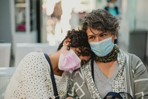 A woman rests her head on the shoulder of another woman, both wearing masks, in a breast cancer clinic in Mexico.