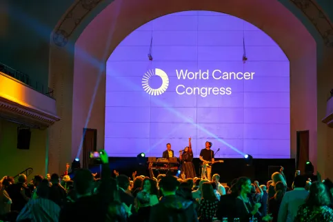 Band sings in front of a crowd, backlit by a purple screen with the words "World Cancer Congress". Social event at the World Cancer Congress