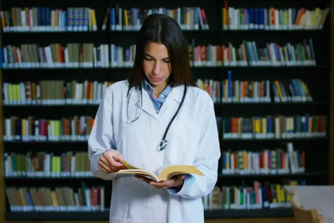 Woman doctor reading a book in a library, illustrating the publication of the 7th edition of the TNM Atlas based on the UICC TNM Classification of Malignant Tumours