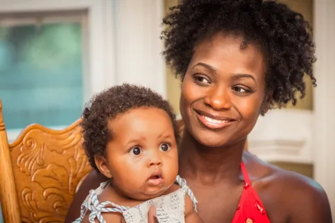 Black woman smiling, with child on her lap. Photo by Andrae Ricketts on Unsplash.