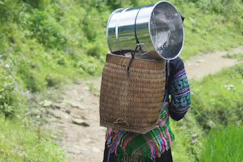Three women carrying baskets on their back, walking on a mountain trail 