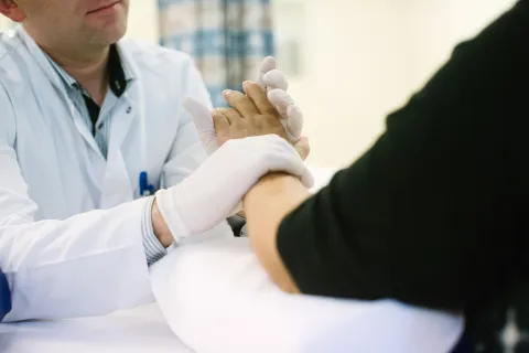 Male doctor wearing sterilised gloves holding the hand of a Caucasian woman patient