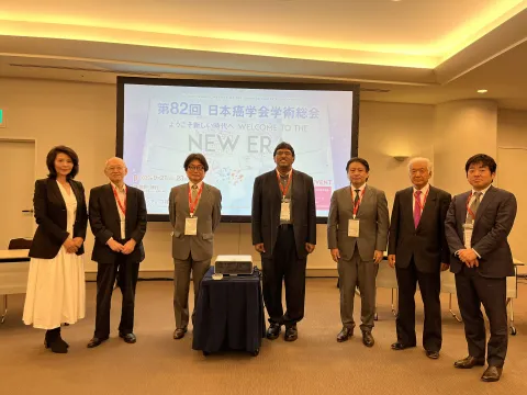 Seven men and women posing for a picture in front of a LED screen