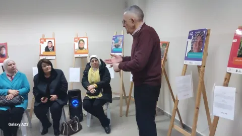 Participants sitting on chairs at an exhibit to give voices to people with cancer listening to a doctor