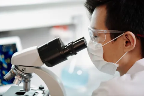 Asian man wearing a mask looking into microscope