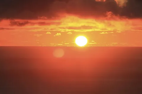 Hot sun setting on the horizon, sky reddish orange
