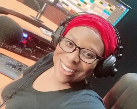 Black woman with red headscarf and wearing headphones smiles to the camera