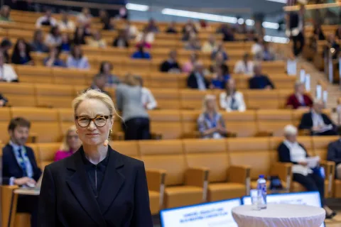 Scandinavian blond woman with glasses standing with her back to an auditorium.