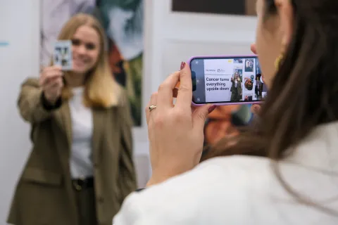 Young blond haired women showing a picture of her doing the World Cancer Day upside down challenge while a colleague films for FujiFilms