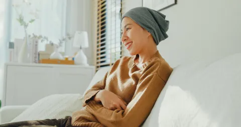 Asian woman with a headscarf smiling, seated on a sofa