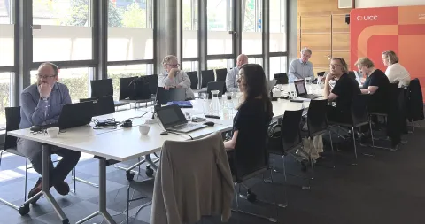 Diverse group of people sitting around a conference table, in the background branded UICC poster