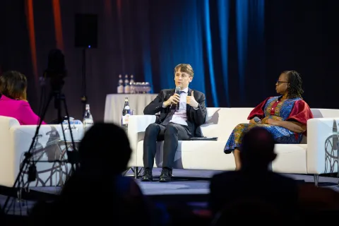 White male and Black woman on a couch on a stage giving a presentation