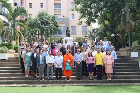 Diverse group of people standing on steps in front of a building surrounded by palm trees, in Bangkok