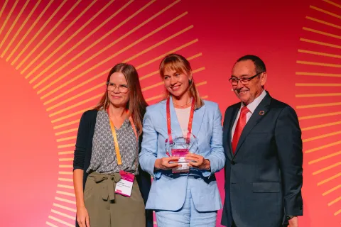Two women and a man in suit receiving an award on stage