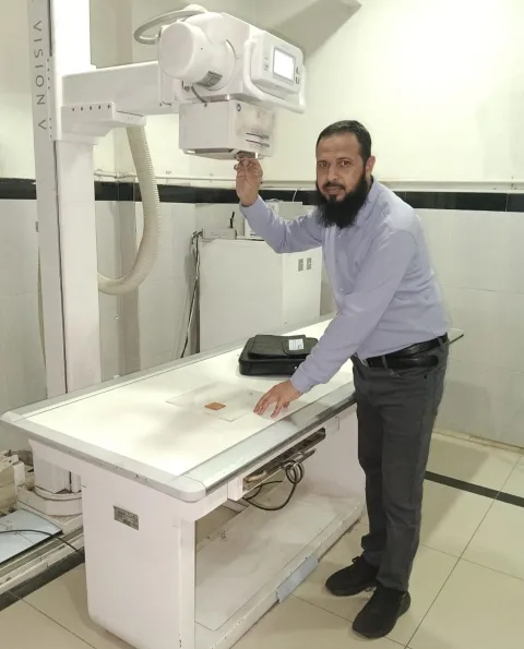 Middle Eastern man in shirt and trousers in front of a radiotherapy machine