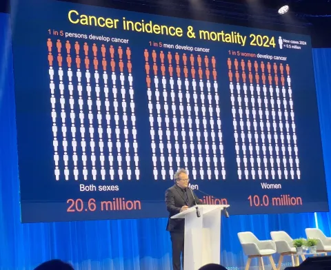 Man at podium giving a slide show presentation of cancer incidence and mortality