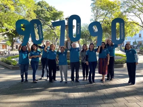Personal de la Liga Nacional Contra el Cáncer Guatemala sosteniendo carteles con números para deletrear los objetivos de la OMS para la eliminación del cáncer de cuello uterino en 2030: 90, 70, 90.