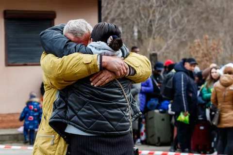Refugees from Ukraine at the border at Uzhgorod-Vyshne Nemeckoe, 26 February 2022. Fotoreserg/Depositphotos.com. Man and women hugging before a line of Ukrainian refugees