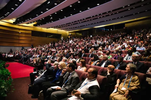 People seated in an auditorium listening to a session on cancer control