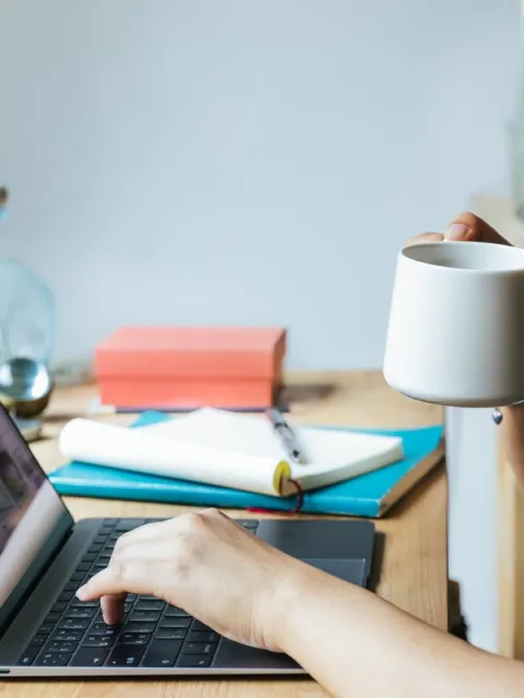 Asian woman on her laptop smiling and drinking coffee