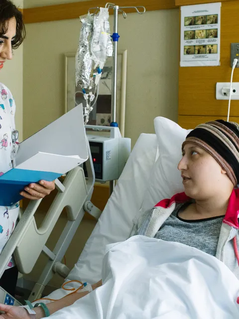 Women healthcare provider talking to a cancer patient lying in a hospital bed, holding a file in her hands