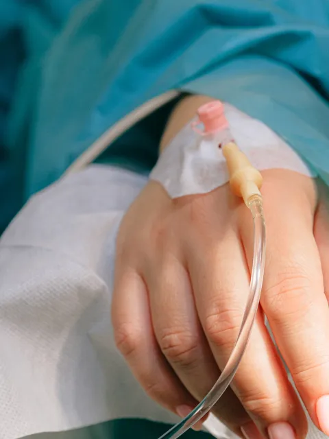 Close up of IV drip in a white hand lying on a hospital bed