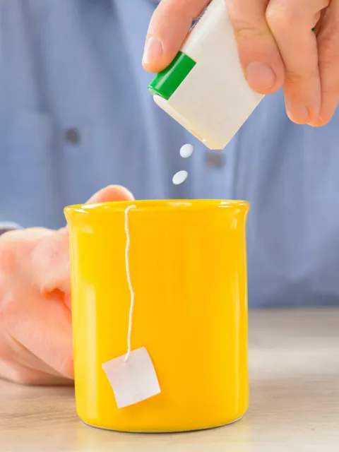 Man pours artificial sweetener containing aspartame into his tea. 