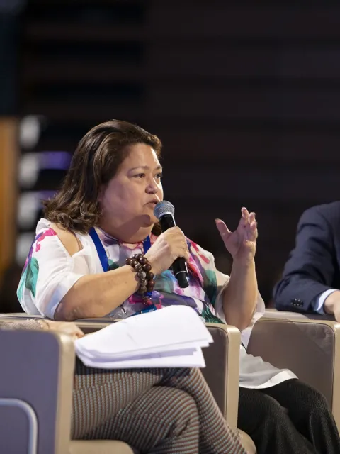 Carmen Auste, CEO of Cancer Warriors Philippines speaking at a conference panel with two men on either side of her