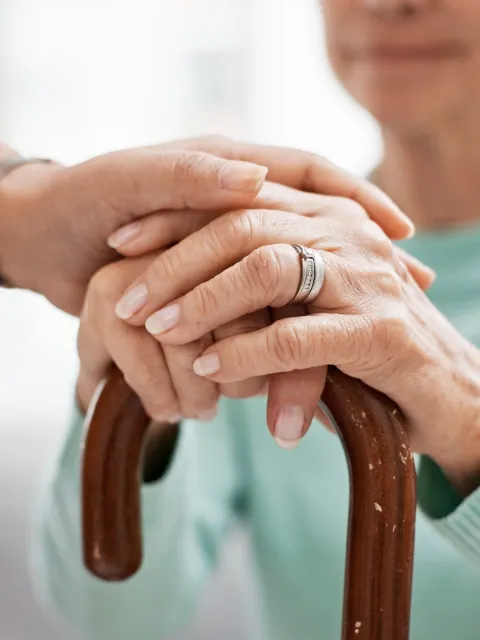 A young white hand clasping an older white hand resting on top of a cane