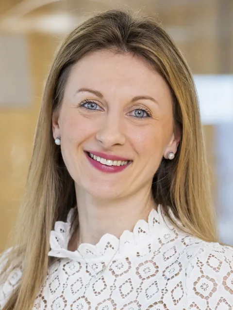 Headshot of white woman with long hair wearing white blouse, Tamara Schudel, Global Head Policy, Roche Pharmaceuticals