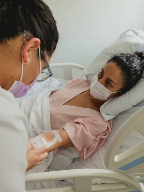 Woman lying in bed wearing a mask receiving IV treatment for cancer