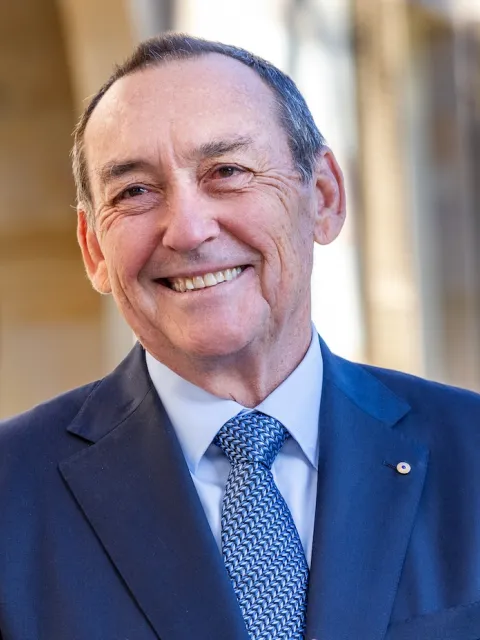 Headshot of Prof. Jeff Dunn, AO, President of UICC (2022-2024), in blue suit and tie, clasping hands in front of him