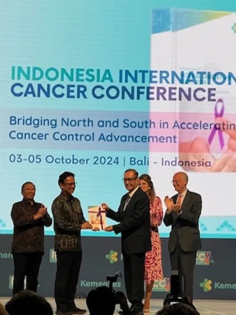 Two Asian men in suits receiving an award on stage at a cancer conference in Indonesia