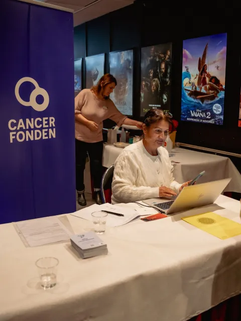 Swedish Cancer Society booth at a move theater, a woman sitting down is taking details from a customer