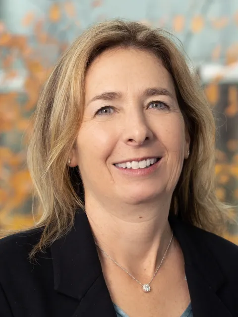 Headshot of a blond woman with shoulder-length hair wearing a necklace and dark suit