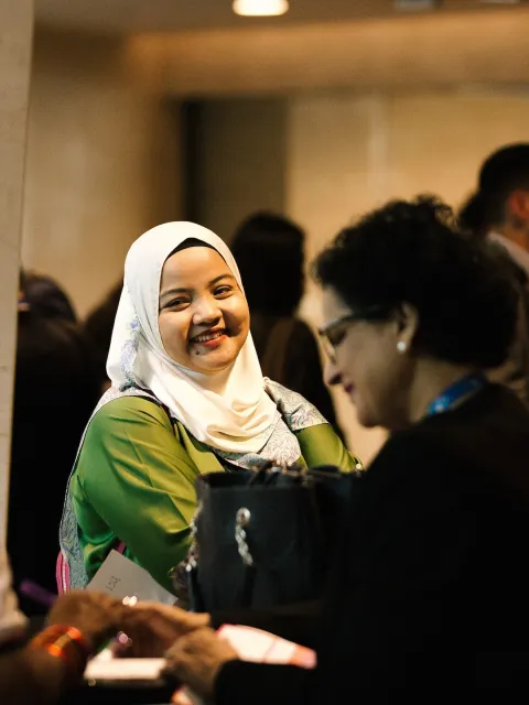 Several people at an event in discussion, focus on a woman wearing a headscarf