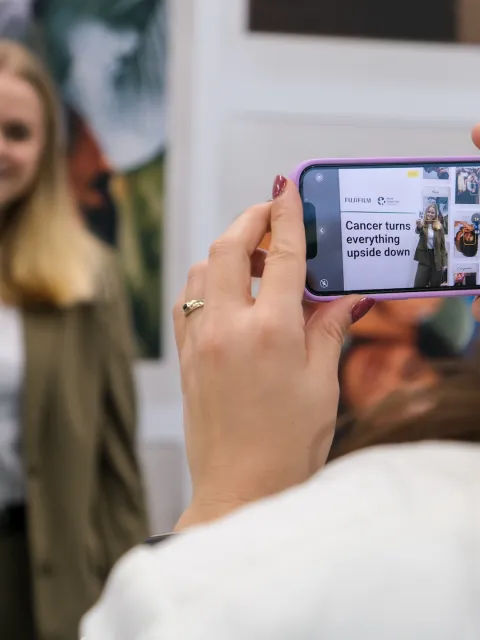 Young blond haired women showing a picture of her doing the World Cancer Day upside down challenge while a colleague films for FujiFilms
