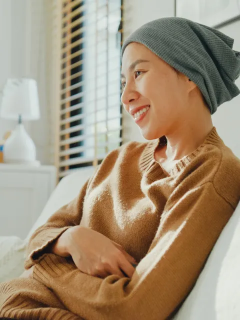 Asian woman with a headscarf smiling, seated on a sofa