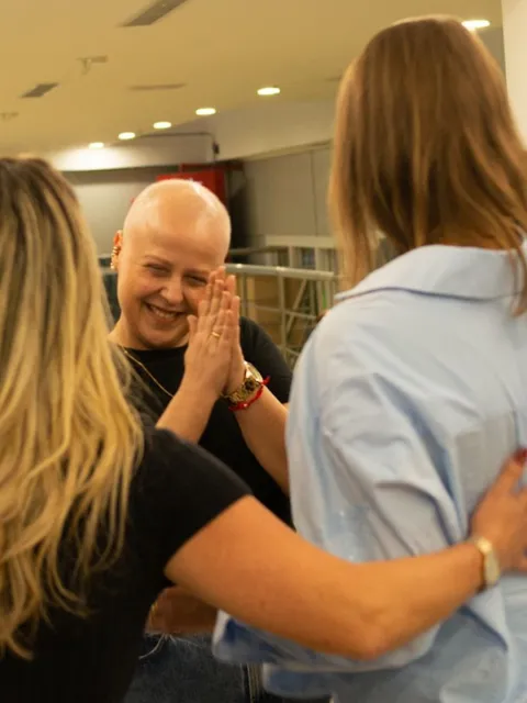 Diverse group of people huddling in a group, one woman without hair clapping