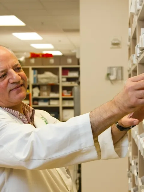 Older white male wearing white lab coat taking medicine from a shelf