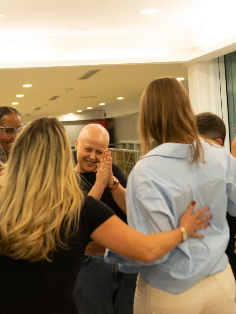 Diverse group of people huddling in a group, one woman without hair clapping