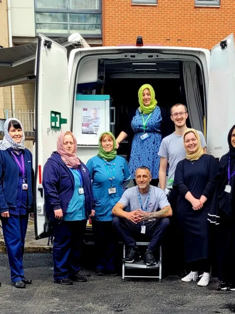 A Caucasian man with women wearing headscarves working for the World Hepatitis Alliance posing before a service van